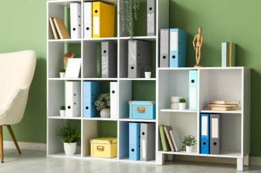 Ofiste yeşil duvarın yanında doküman klasörleri ve bitkilere sahip raflar