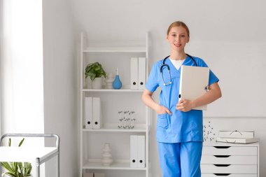 Klinikte steteskoplu ve klasörlü mutlu kadın doktor.