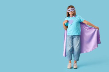 Mavi arka planda süper kahraman gibi giyinmiş genç bir kız.