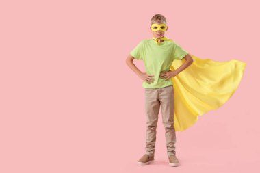 Pembe arka planda süper kahraman gibi giyinmiş genç bir çocuk.