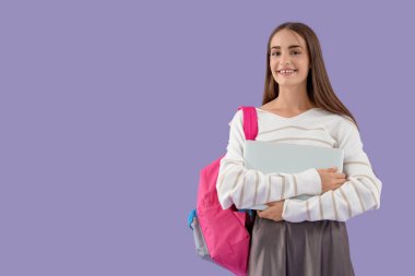 Mor arka planda sırt çantası ve dizüstü bilgisayarı olan mutlu bir kız öğrenci.