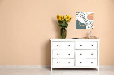 İçinde güzel ayçiçekleri olan vazolar, heykelcikler ve oturma odasındaki çekmecelerin üstündeki dergiler.