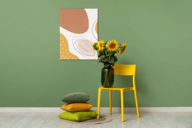Oturma odasındaki yeşil duvarın yanında, üzerinde güzel ayçiçekleri olan yastıklar ve vazolar.