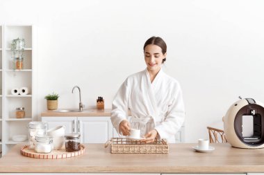 Bornozlu genç bayan evdeki tepsiye bir fincan kahve koyuyor.