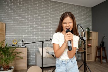 Evde mikrofonlu küçük bir kız şarkı söylüyor.