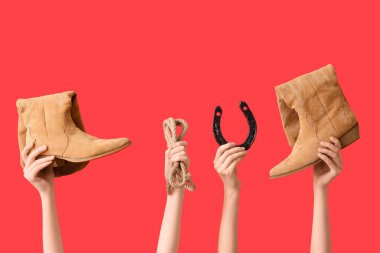 Kırmızı arka planda şık kovboy ayakkabıları, at nalı ve kement olan kadın elleri.