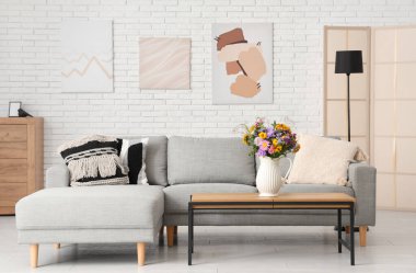 Oturma odasındaki sehpada yabani çiçekler olan rahat bir kanepe ve vazo.