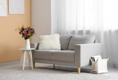 Oturma odasındaki sehpanın üzerinde yabani çiçekler olan kanepe ve vazo