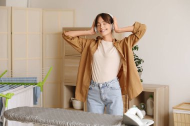 Kulaklıklı mutlu genç kadın çamaşırhanede dans ediyor.