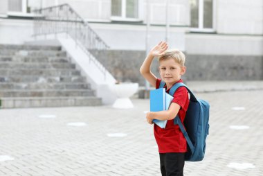 Sırt çantası ve el sallayan kitapları olan sevimli bir çocuk.
