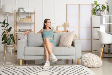 Aydınlık oturma odasındaki gri koltukta oturan genç kadın.