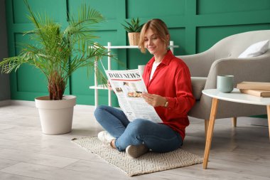 Evdeki koltuğun yanında elinde gazeteyle oturan genç ve güzel bir kadın.