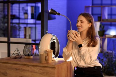 Geceleri elinde bir fincan espresso ve kahve makinesi olan genç bir iş kadını.