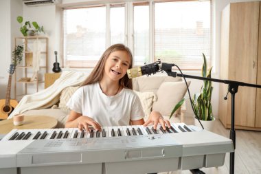 Evde sentezleyici ve mikrofon şakıyan küçük kız.