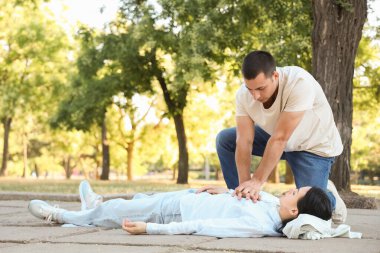 Genç adam kalp masajı yapıyor. Baygın karısı parkta kalp krizi geçiriyor.