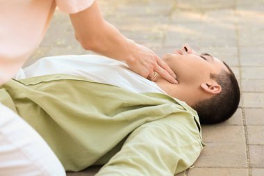 Genç bir kadın kalp krizi geçiren baygın bir adamın nabzını kontrol ediyor.