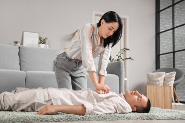 Genç bir kadın evde kalp krizi geçiren baygın bir kocaya kalp masajı yapıyor.