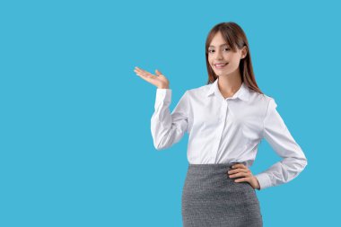 Güzel genç iş kadını mavi arka plandaki bir şeyi işaret ediyor.