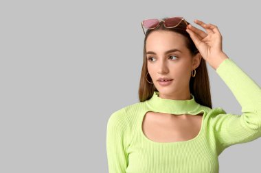 Gri arka planda pembe güneş gözlüklü güzel bir genç kadın.