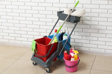 Beyaz tuğla duvarın yanında temizlik malzemeleri olan bir tramvay.