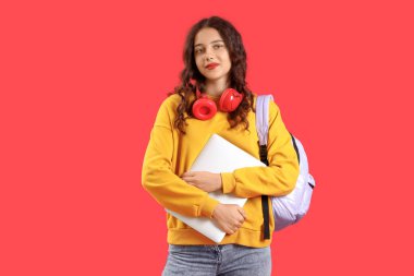 Kırmızı arka planda dizüstü bilgisayarı olan kız öğrenci.