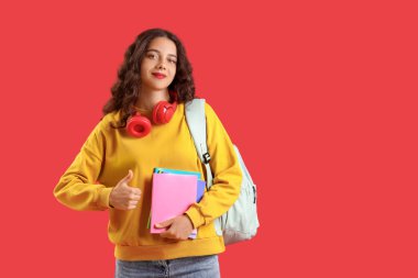 Fotokopi kitapları olan kız öğrenci kırmızı arkaplanda başparmağını kaldırıyor