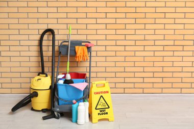 Temizlik malzemeleri, uyarı levhası ve tuğla duvarın yanındaki elektrikli süpürge.