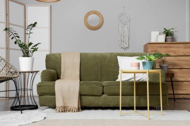 Ayna, yeşil kanepe ve masalarla aydınlık oturma odasının içinde.