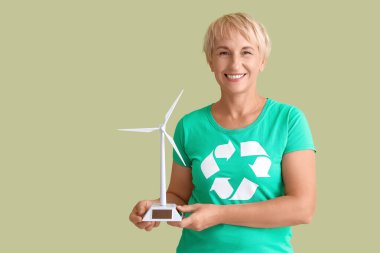 Tişörtünde geri dönüşüm işareti ve yeşil arka planda rüzgar türbini modeli olan olgun bir kadın.