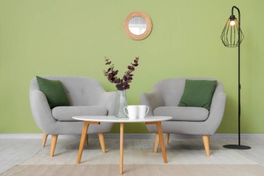 Oturma odasının içinde ayna, gri koltuklar ve masa var.