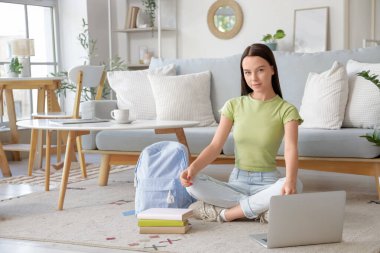 Bayan öğrenci evde yerde ders çalışıyor.