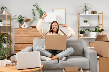 Güzel, genç, mutlu bir kadın. Bir sürü koli ve dizüstü bilgisayarı var. Evde oturuyor.