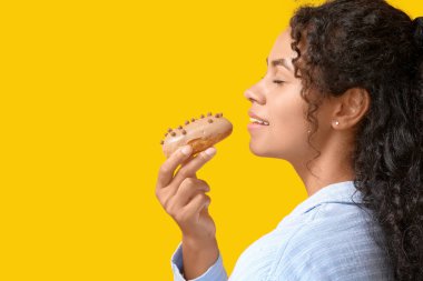 Afro-Amerikalı bir kadın sarı arka planda lezzetli ekinler yiyor.