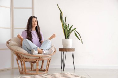 Evdeki rahat koltukta meditasyon yapan güzel bir kadın.