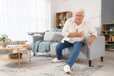 Olgun bir adam evdeki koltukta kalp krizi geçiriyor.