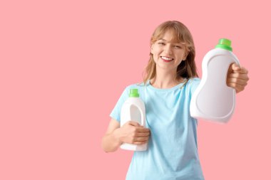 Pembe arka planda çamaşır deterjanı şişeleri olan genç bir kadın.