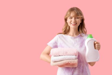 Pembe arka planda bir yığın temiz havlu ve çamaşır deterjanı olan genç bir kadın.