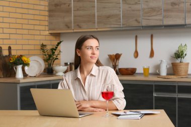 Mutfaktaki masada dizüstü bilgisayar kullanan genç bir kadın.