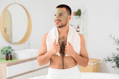 Evdeki banyoda yüzü kozmetik jel maskeli yakışıklı genç adam.