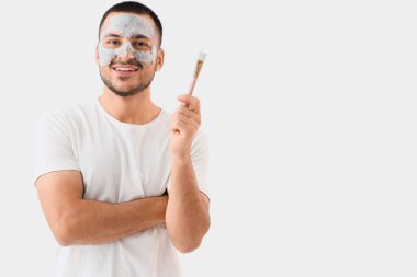 Yüzünde kozmetik balon maskesi ve gri arka planda fırçası olan yakışıklı genç adam.