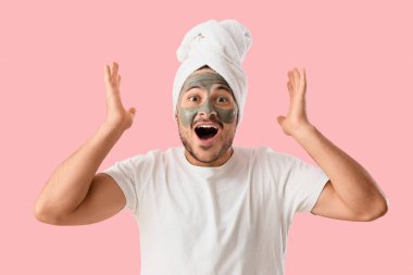 Yüzünde kozmetik kil maskesi olan yakışıklı, genç ve şaşkın bir adam.