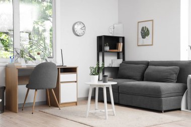 İçinde modern gri kanepe, sehpa ve çalışma alanı olan oturma odası.