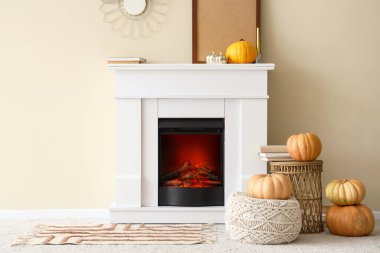 Beyaz şömineli, yumuşak puflu, balkabaklı ve kahve masalı bir oturma odası.