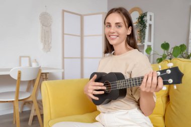 Evdeki kanepede gitar çalan genç bir kadın.