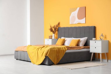 Rahat yataklı, komodinli güzel bir yatak odası, otların resmi ve vazosu.