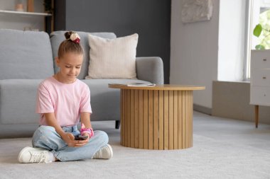 Evde yerde cep telefonu kullanan küçük kız.