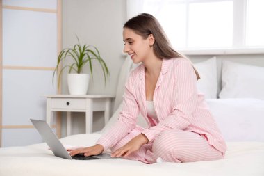 Pijamalı genç bir kadın evde dizüstü bilgisayar kullanıyor.