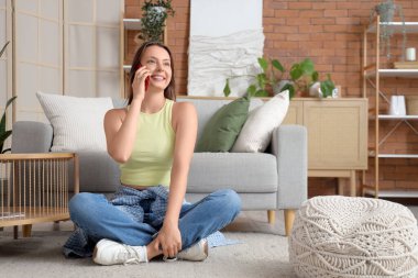 Evde cep telefonuyla konuşan genç bir kadın.
