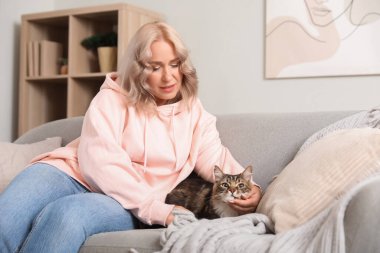 Güzel, olgun, mutlu, tatlı kedisi olan bir kadın evdeki kanepede oturuyor.