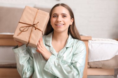Yatak odasında Noel hediyesi kutusuyla mutlu genç bir kadın.